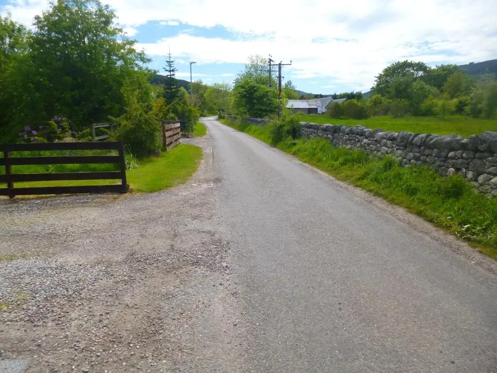 an empty road with a stone wall and a fence at Aslaich in Drumnadrochit