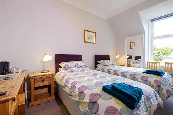 a bedroom with two beds and a wooden desk at Eastdene Guest House in Inverness