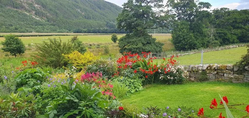 a garden with colorful flowers and a stone wall at Clachan Farmhouse B & B in Ullapool
