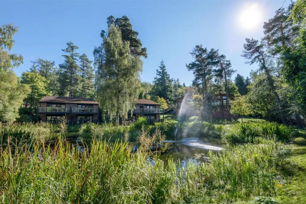 a garden with houses and a pond with a fountain at Hilton Grand Vacations Club Craigendarroch Suites Scotland in Ballater