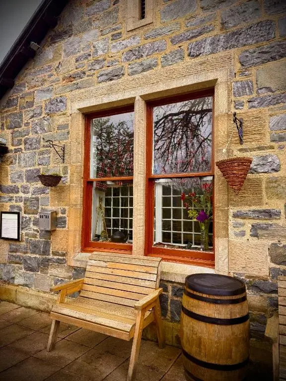a wooden bench in front of a stone building with a barrel at Loch Ness Lodge Hotel in Drumnadrochit
