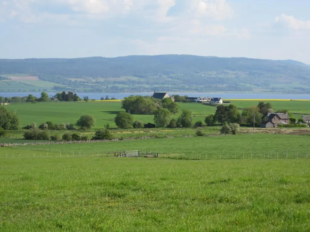 a field of green grass with a house in the distance at Kilcoy Chalets in Muir of Ord