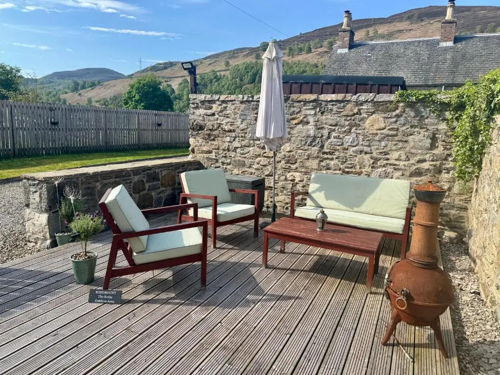 a patio with chairs and an umbrella on a wooden deck at Rosemount Bothy - Highland Cottage in Garve