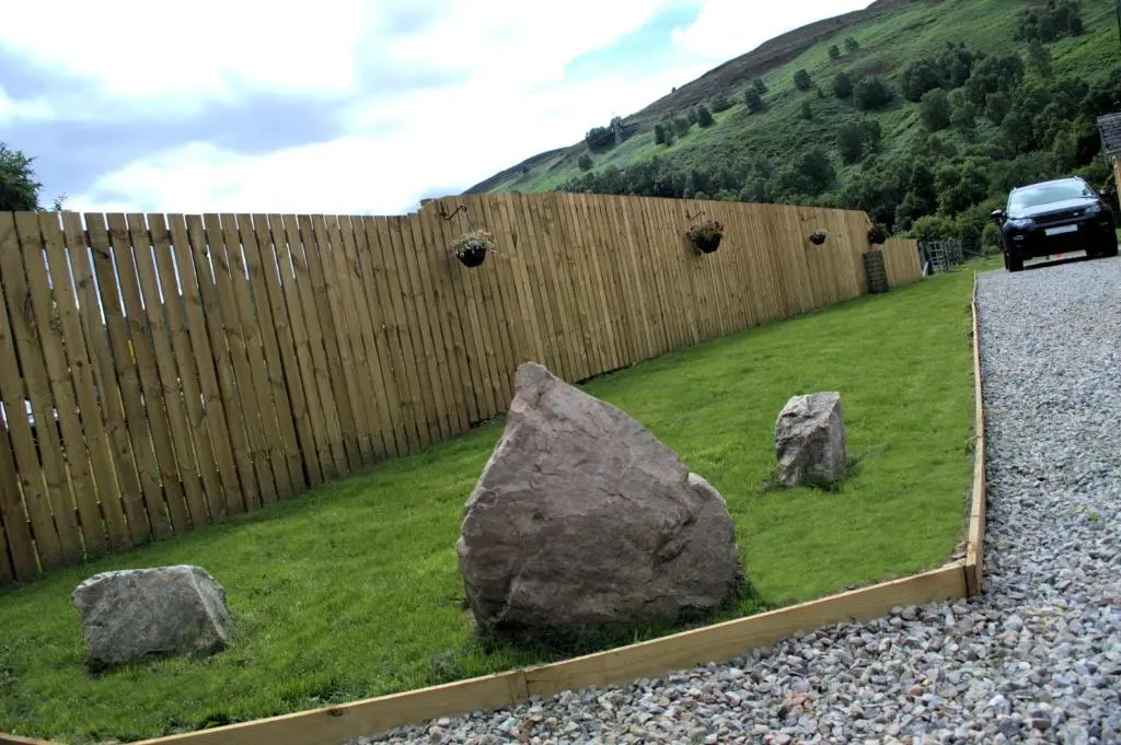two large rocks in the grass next to a fence at Rosemount Bothy - Highland Cottage in Garve