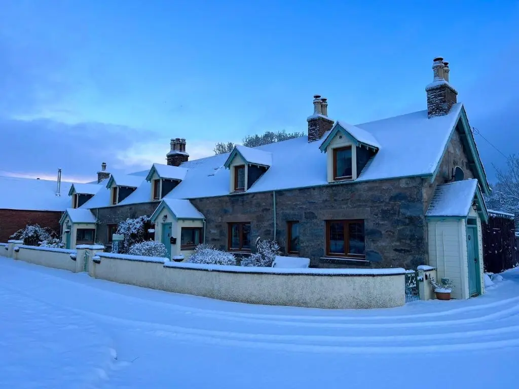 a house covered in snow with a fence at Rosemount Bothy - Highland Cottage in Garve