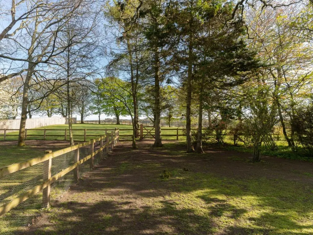 a wooden fence in a field with trees at Garden Cottage in Tain