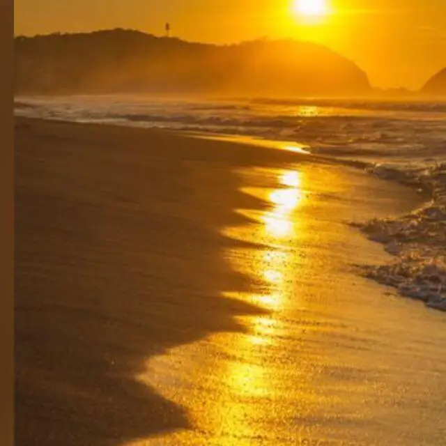a beach with the sun setting in the ocean at Ceol Na Mara Cottage by the sea in Nairn