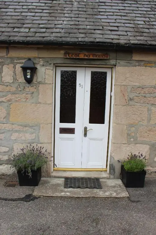 a white door on a stone building with two plants at Ceol Na Mara Cottage by the sea in Nairn