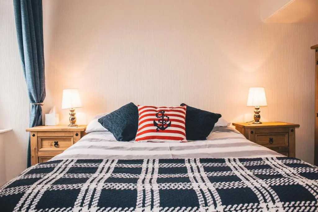 a bed with a blue and white blanket and two lamps at The Mouries Holiday Cottage in Fochabers