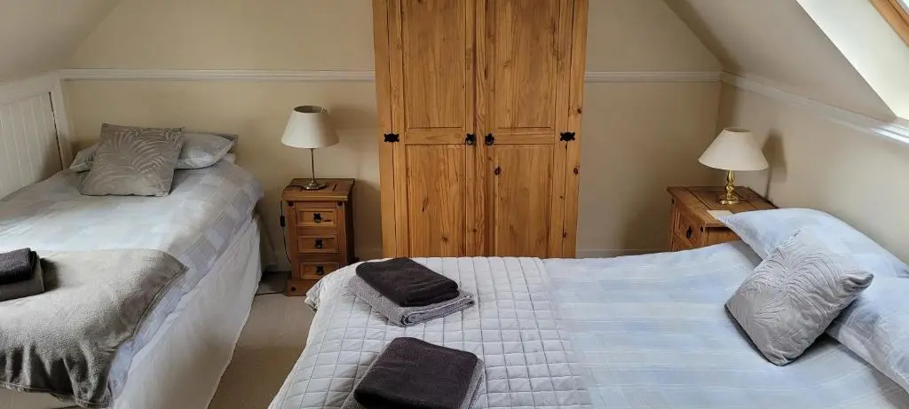 a bedroom with two beds and a wooden cabinet at The Mouries Holiday Cottage in Fochabers