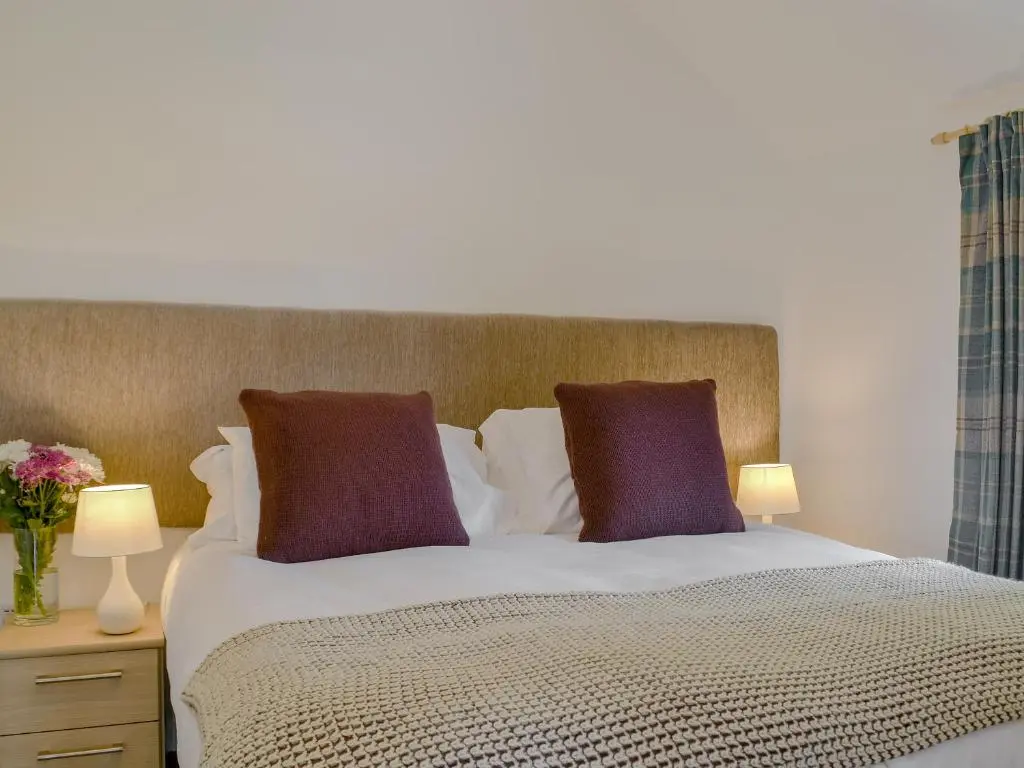 a bed with two purple pillows and two lamps at Wester Laggan Cottage in Skye of Curr