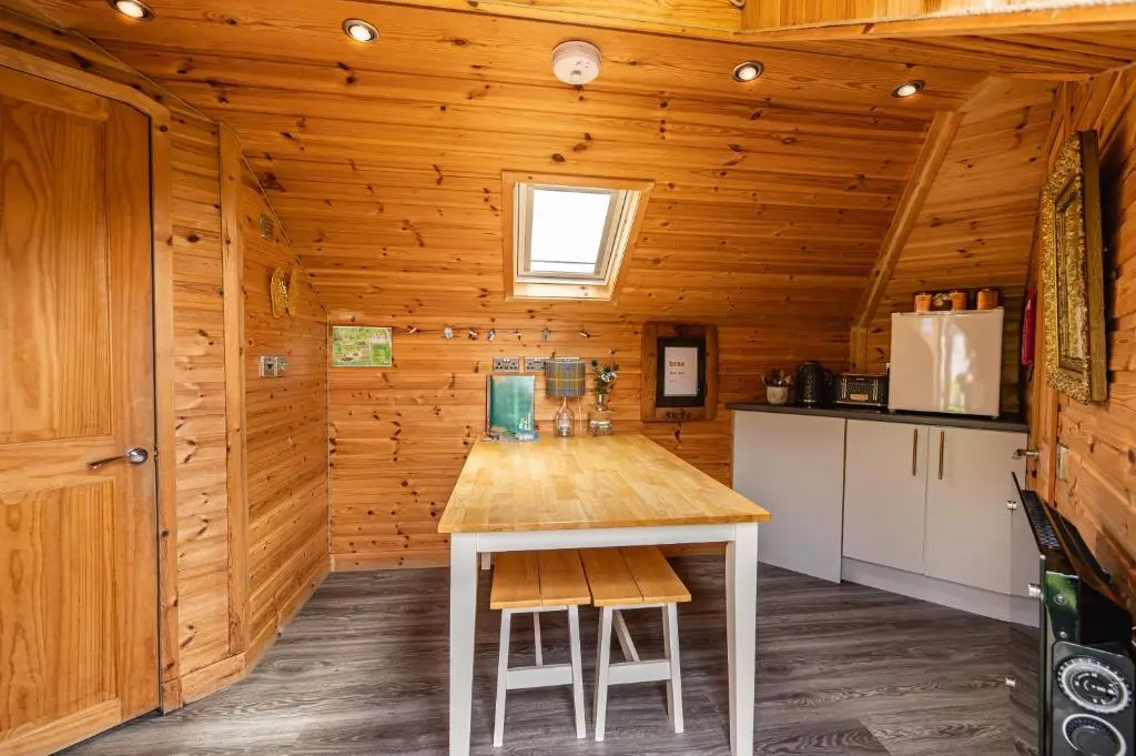 a kitchen with a wooden wall with a table and chairs at Delny Glamping and Farm Animals in Invergordon