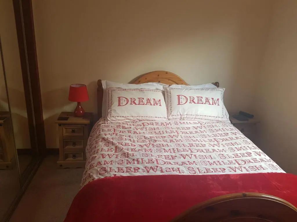 a bedroom with a bed with red sheets and white pillows at Culduthel Vista Apartment in Inverness