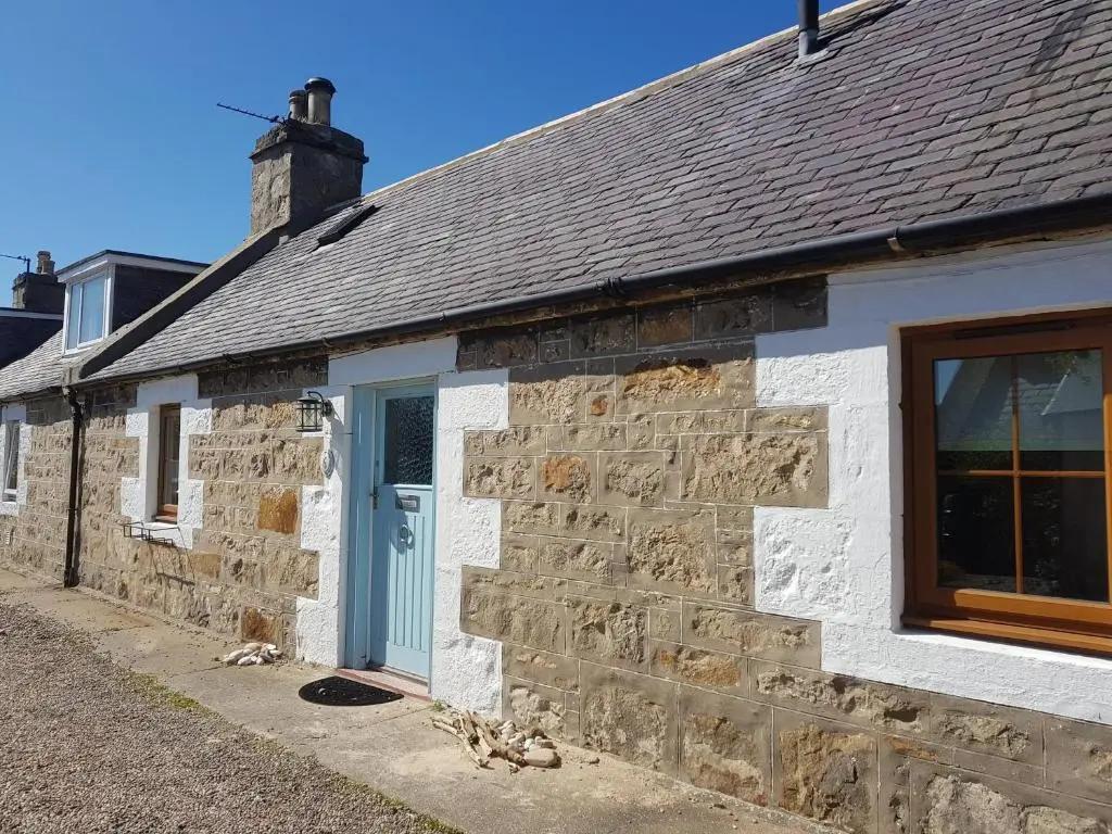 a stone cottage with a blue door and a stone wall at 6 Seatown, Lossiemouth in Lossiemouth