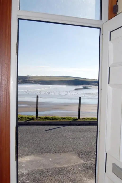 a door with a view of the ocean from a beach at Sandend Cottage in Banff