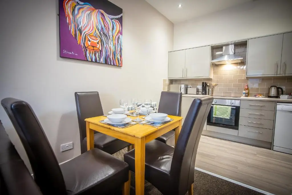 a kitchen with a wooden table with chairs and a dining room at Douglas House Apartments in Nairn