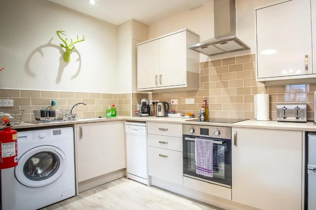 a kitchen with white cabinets and a washer and dryer at Douglas House Apartments in Nairn