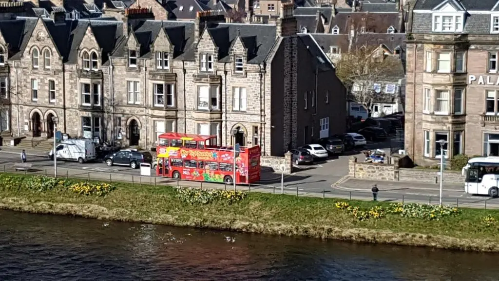 a red double decker bus parked next to a river at 37 Farraline Court, City Centre apartment in Inverness