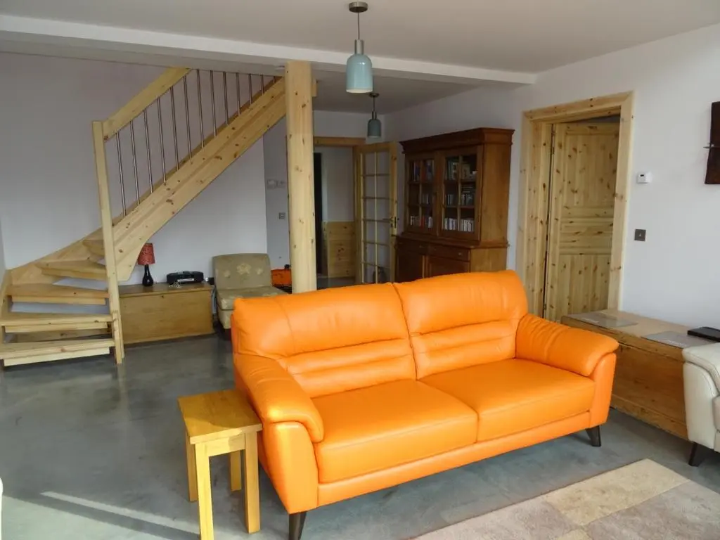 an orange couch in a living room with a staircase at The Loft at Log Ness in Foyers