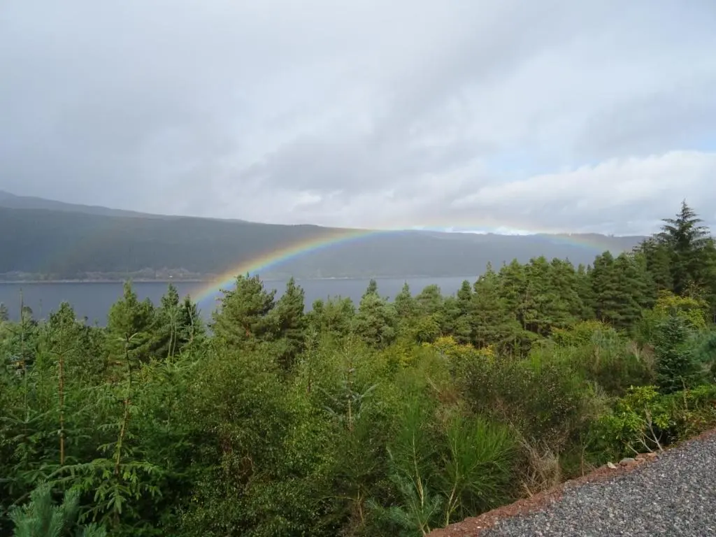 a rainbow over a body of water with trees at The Loft at Log Ness in Foyers