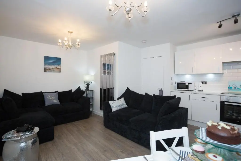 a living room with two black couches and a kitchen at Seaesta Apartments in Macduff