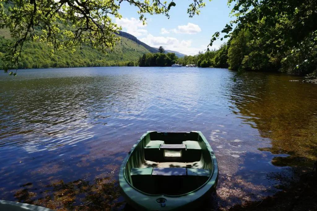 a green boat sitting on the shore of a lake at Glengarry Castle Hotel in Invergarry