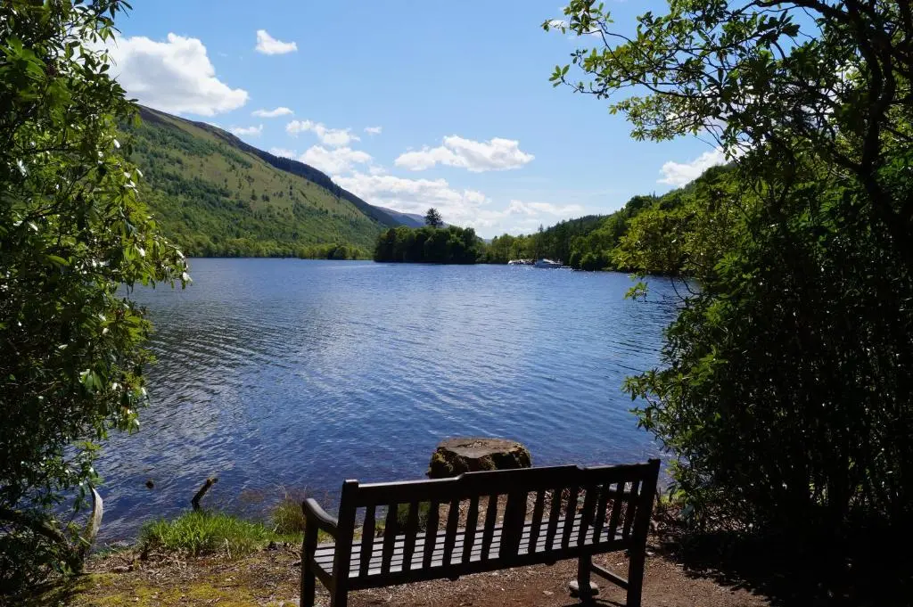 a bench sitting on the shore of a lake at Glengarry Castle Hotel in Invergarry