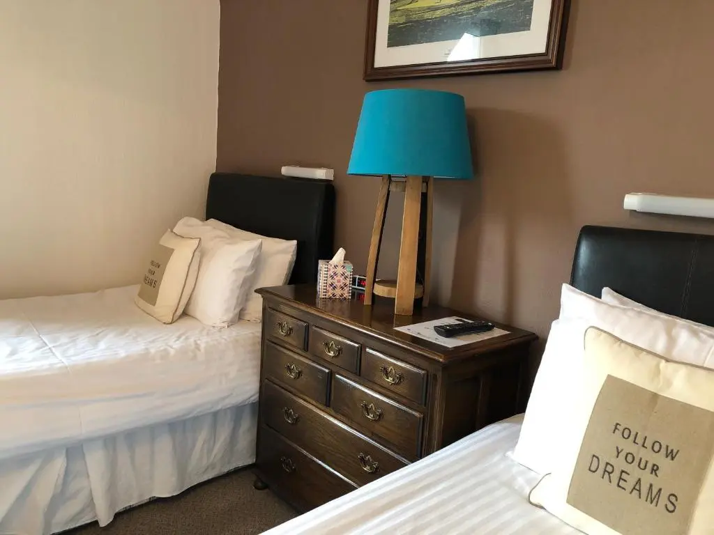 a bedroom with two beds and a blue lamp on a dresser at Westerlea Hotel Nairn in Nairn