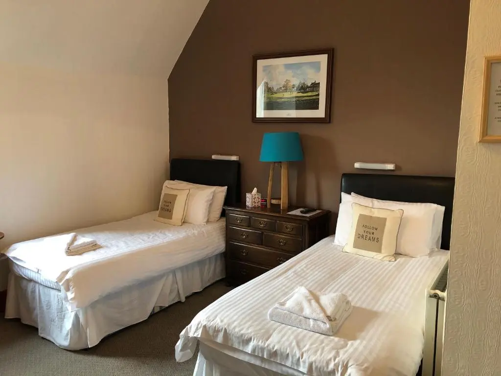 a bedroom with two beds with white sheets and a blue lamp at Westerlea Hotel Nairn in Nairn