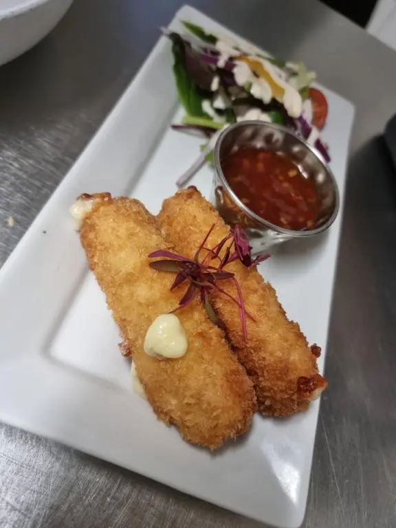 a white plate with fish sticks and a bowl of sauce at Grampian Hotel in Keith