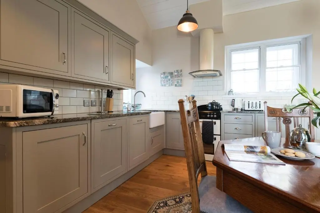 a kitchen with white cabinets and a wooden table at Evelix, The Old School House in Muir of Ord