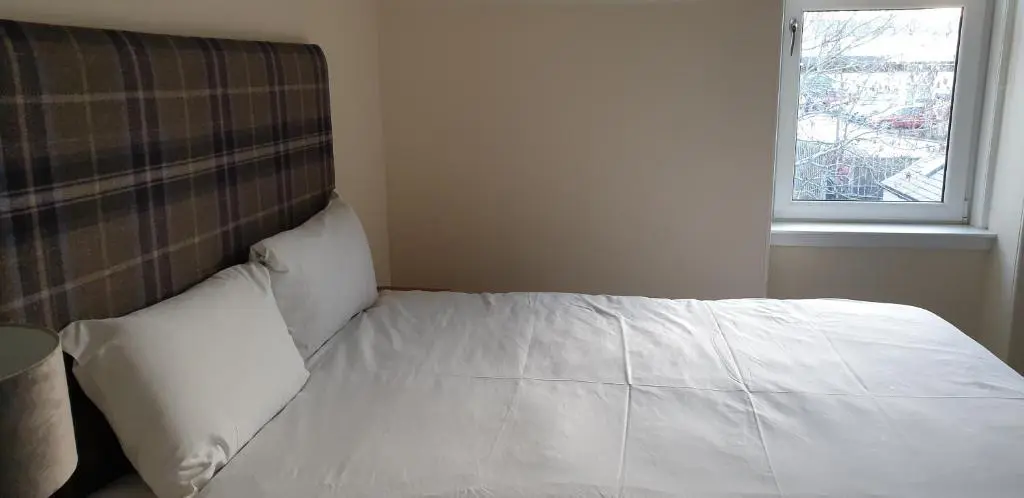 a bedroom with a bed with white sheets and a window at SPRINGBANK Holiday Home in Inverness