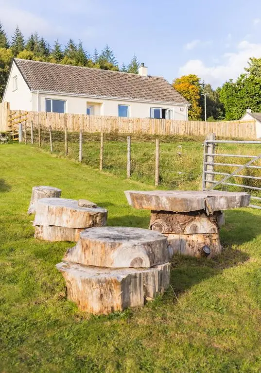 a group of logs sitting in a field next to a fence at Loch Ness Cottage in Fort Augustus