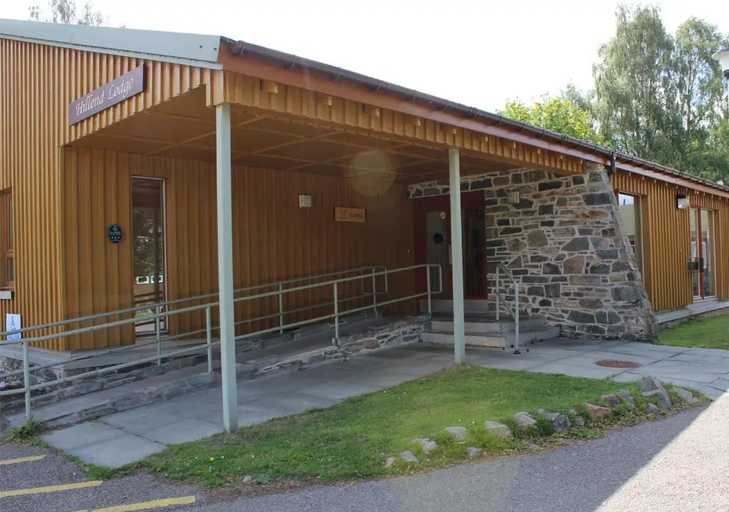 a building with a stone wall and a door at Lagganlia Lodges and Camping Pods in Kincraig