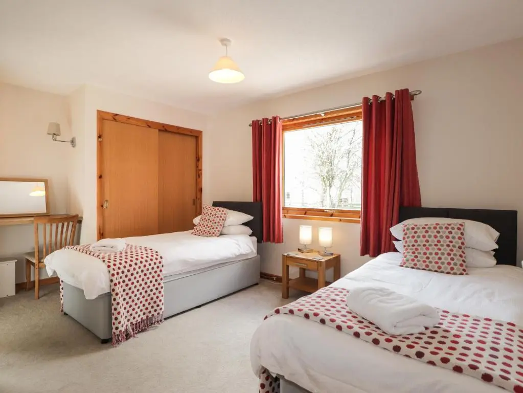 a bedroom with two beds and a window with red curtains at Millview in Boat of Garten