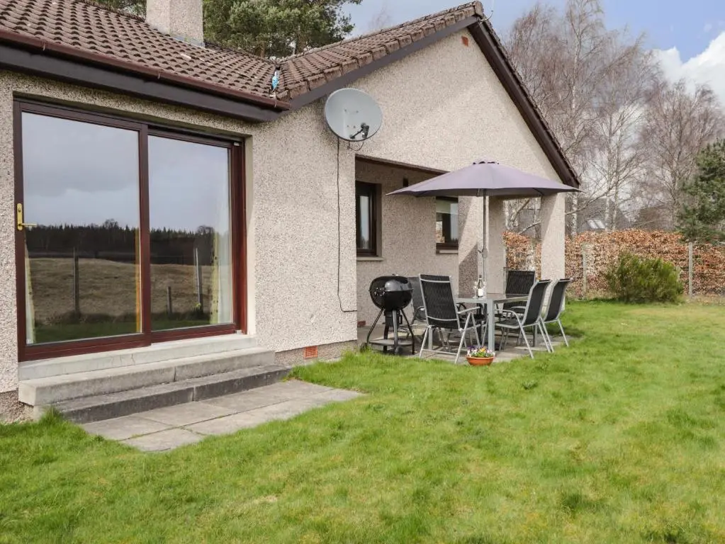 a table and chairs with an umbrella in a yard at Millview in Boat of Garten