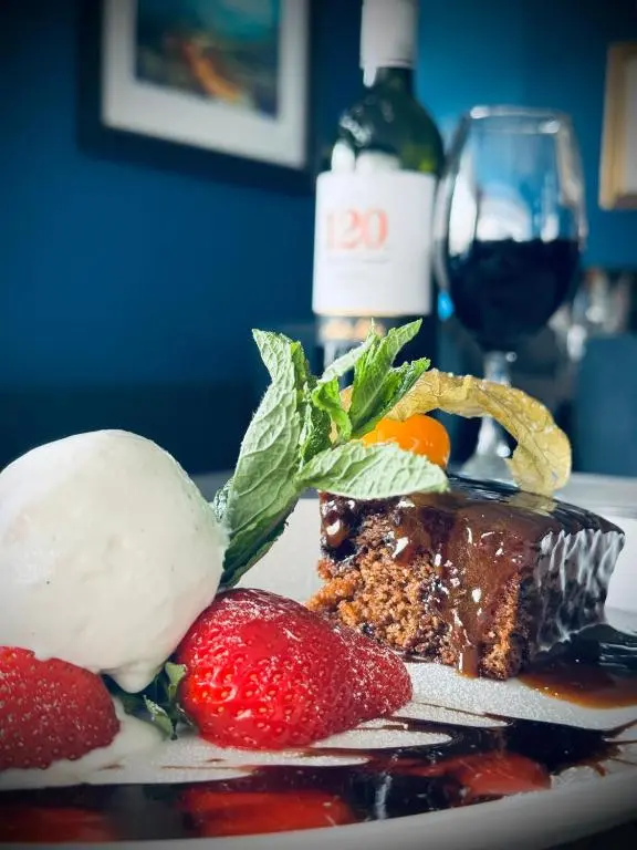 a piece of cake and strawberries on a plate with a glass of wine at Star Hotel Kingussie in Kingussie