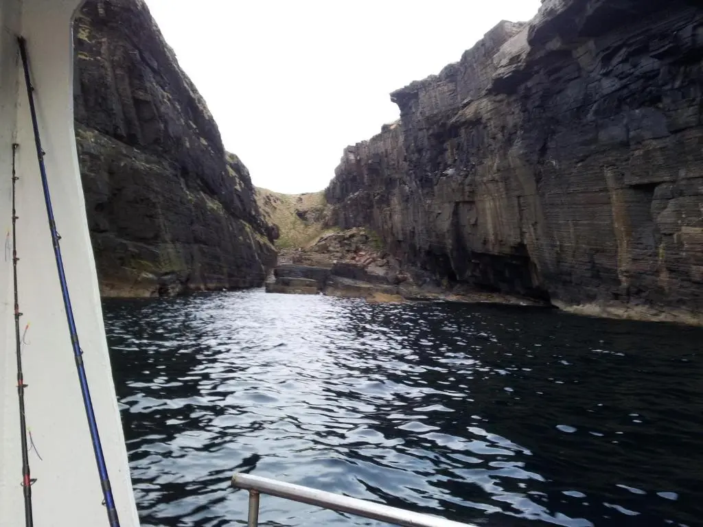 a boat in the water between two cliffs at Harbour House Bed & Breakfast - Wick in Wick