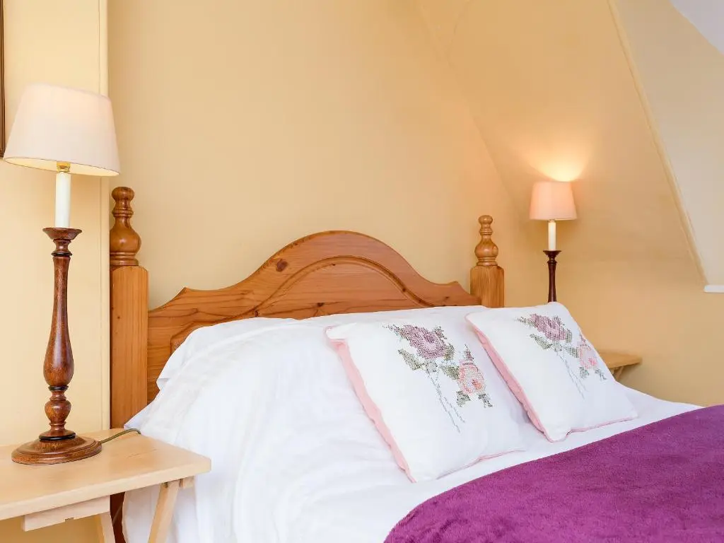 a bedroom with a bed with white sheets and pink pillows at Big Barns Cottage in Backies