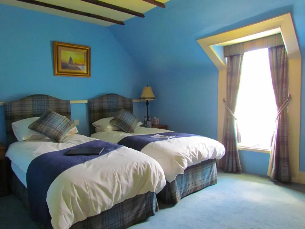 a blue bedroom with two beds and a window at Altnaharra Hotel in Lairg