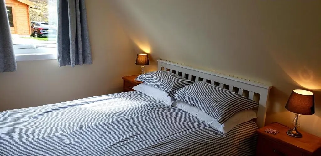a bedroom with a bed with two lamps and a window at Highland Glen Lodges in Rogart