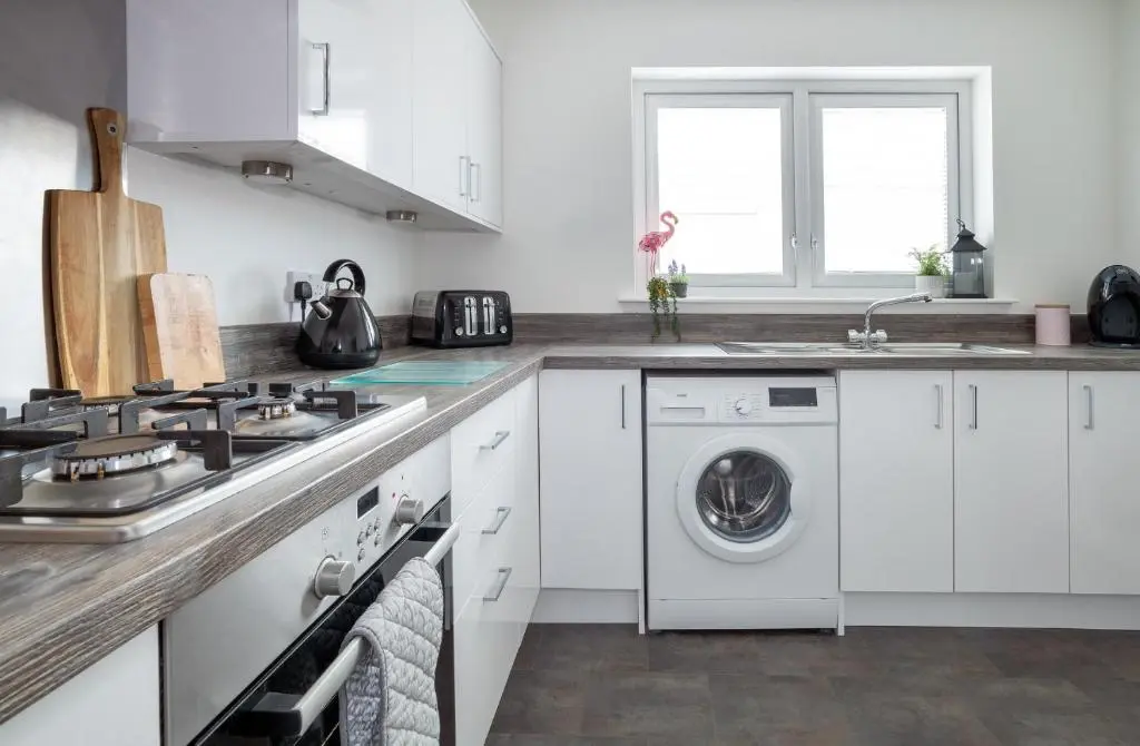 a kitchen with white cabinets and a washer and dryer at Lily Bank House in Inverness