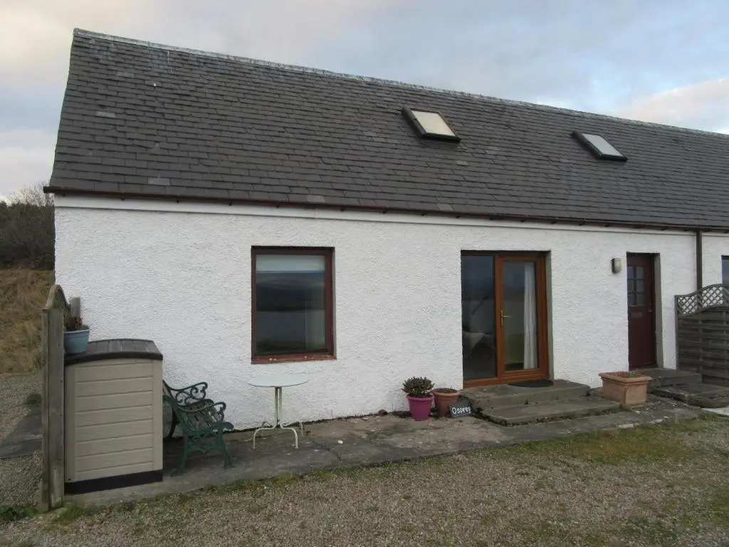 a white house with a bench and a table at Osprey, Longhouse Cottages in Rosemarkie