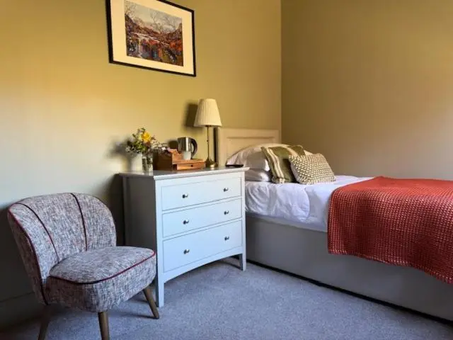 a bedroom with a bed with a dresser and a chair at Ardvreck House in Ullapool