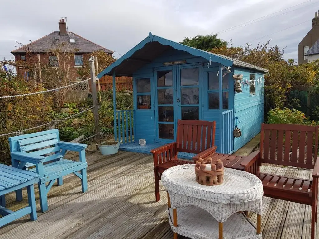 a blue shed sitting on a deck with benches at Driftwood Cottage, Portsoy in Banff