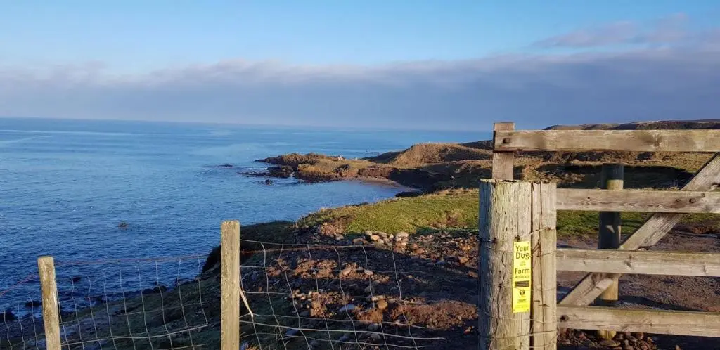 a fence on a cliff next to the ocean at Driftwood Cottage, Portsoy in Banff