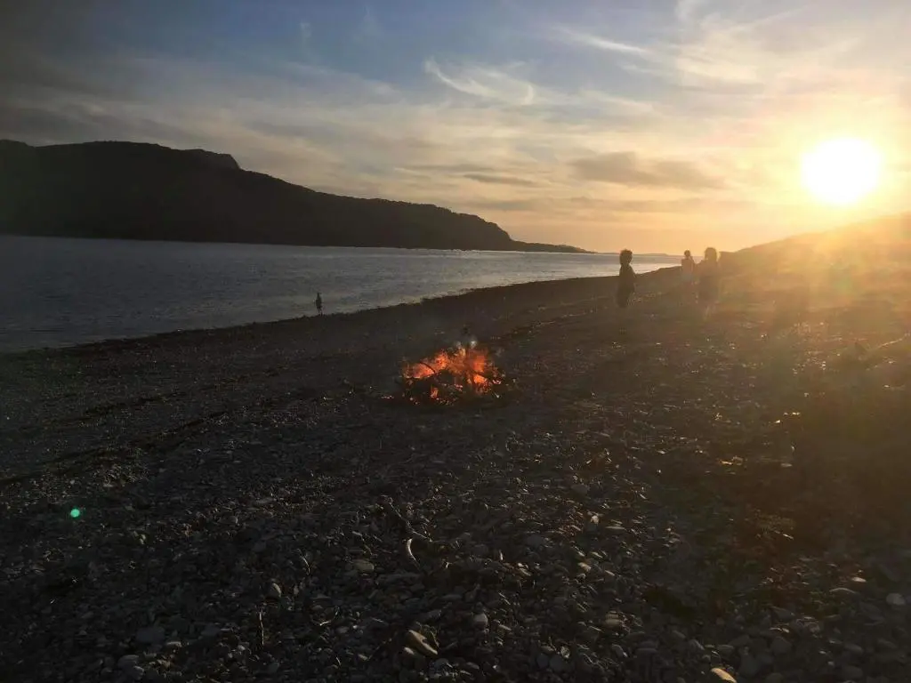 a group of people standing on a beach next to a fire at Croft No.8 Bed & Breakfast in Ullapool