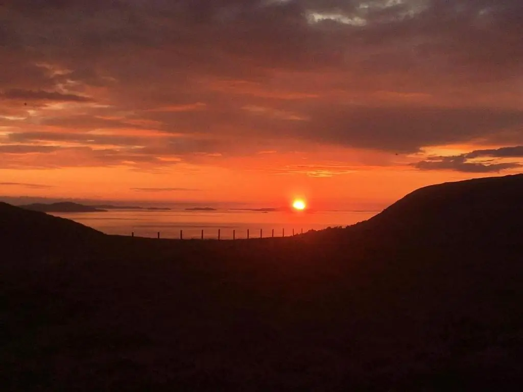 a sunset over a hill with a fence at Croft No.8 Bed & Breakfast in Ullapool