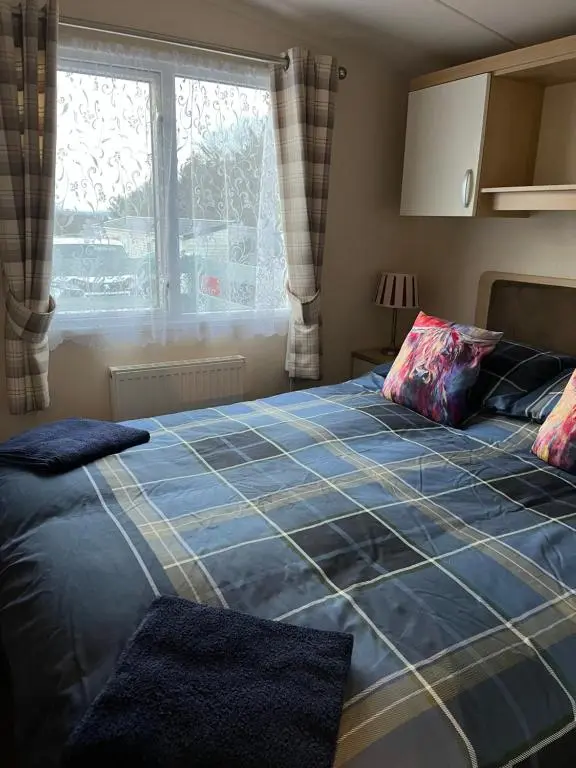 a bedroom with a bed with a blue blanket and a window at Braemar in Dornoch