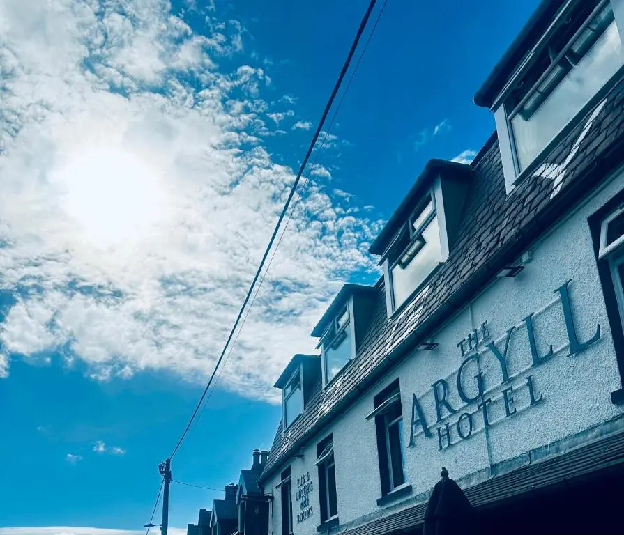 a building on a street with the sun in the sky at Argyll Hotel in Ullapool